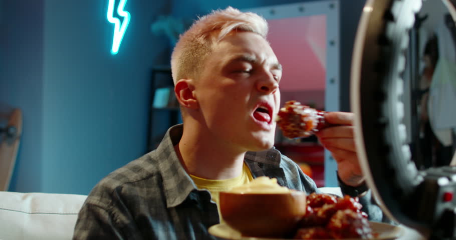 Male blogger eating chicken for video. Man eats super spicy chicken legs for video on Internet social network. Difficult challenge tasting of burning peppery spicy foods for video. Challenge endurance Royalty-Free Stock Footage #1108047817