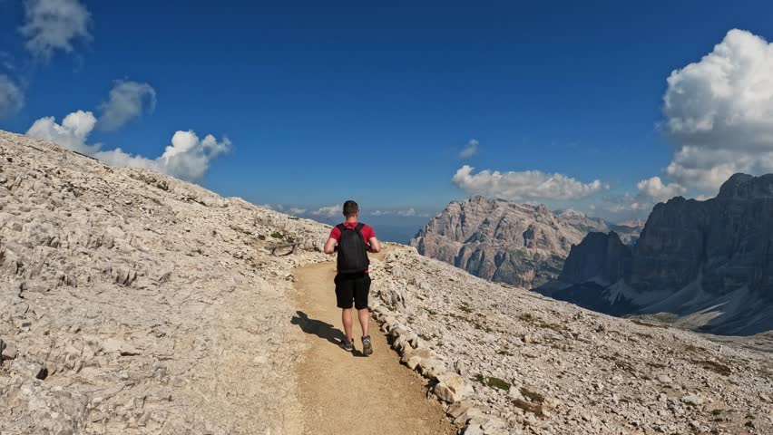 Active man with backpack hiking and climbing Dolomites mountain. Summer adventure journey in nature outdoors. Travel exploring Alps, Dolomites, Italy