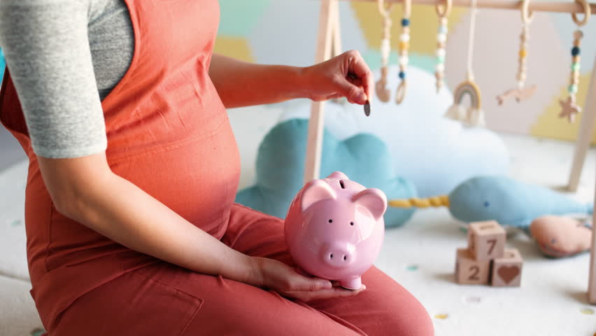 Pregnancy family planning budget. Cost of having a child. Pregnant woman putting money in piggy bank shopping newborn toys and nursery decor with savings. Maternity leave benefits. Royalty-Free Stock Footage #1108053473