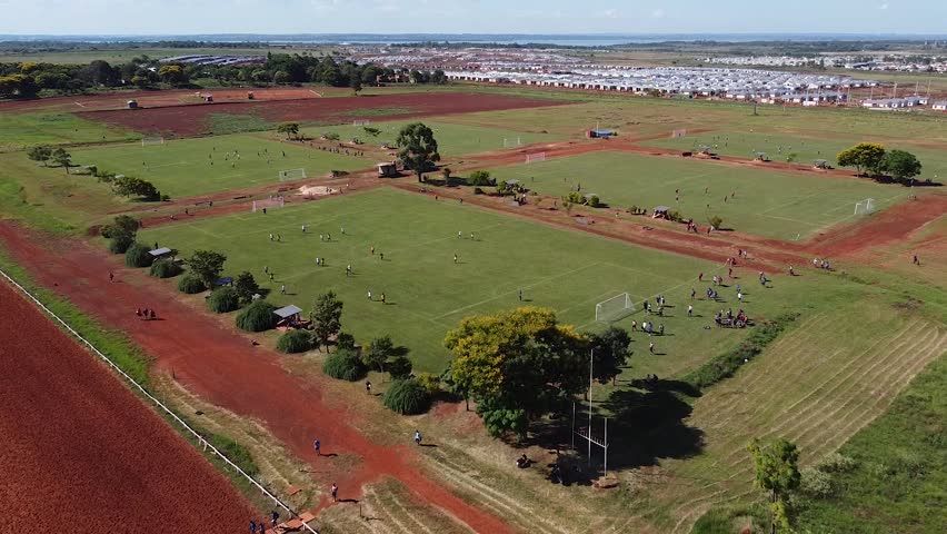 Drone retreat from football matches being played revealing surrounding countryside - people walk away from field - Posadas hipodrome