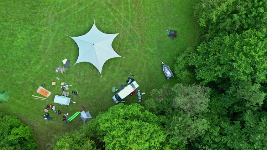 People camping on green meadow with huge tent and van, aerial top down view