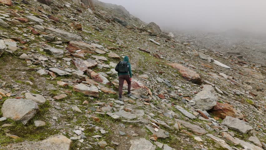 Aerial View Of Lone Hiker Walking Up Along Path On Rocky Mountain Hillside Through Hazy Fog. Circle Dolly Shot
