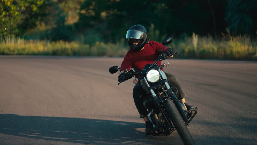 A man in a red sweater and a motorcycle helmet effectively turns on the road on a motorcycle in sunny weather. Motorcycle riding as a hobby Royalty-Free Stock Footage #1108066091
