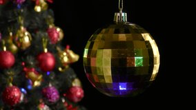 On a black background, a yellow Christmas ball rotates near a decorated Christmas tree