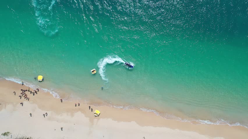 Top down view of outdoor enthusiasts enjoying jet skiing, banana boat riding and other water sports at a beautifu beach on Jibei Island, which is a popular summer holiday destination in Penghu, Taiwan Royalty-Free Stock Footage #1108072117