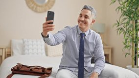 Young hispanic man business worker having video call sitting on bed at hotel room
