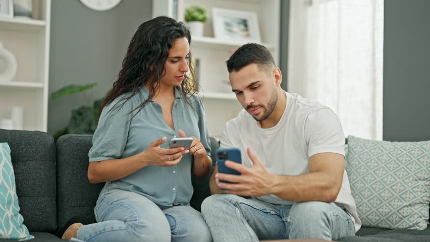 Man and woman couple using smartphones sitting on sofa at home