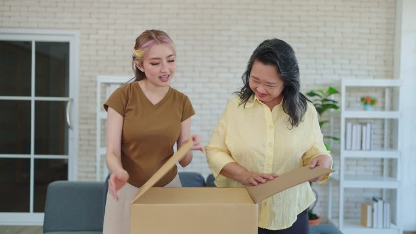 Young Asian woman with mature mother enjoy unpacking parcel together. Happy elderly mom and daughter excited unpacking cardboard box receiving ordered from internet store. Online Shopping | Shutterstock HD Video #1108076853