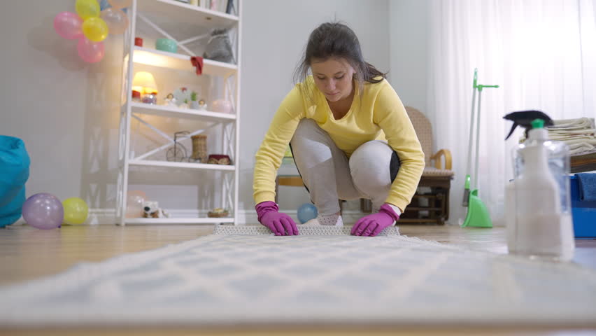 Young woman rolling up carpet in living room indoors and leaving. Portrait of professional service employee cleaning house