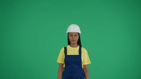 Medium green screen isolated chroma key video of a dark-skinned young female construction worker raising two rolled up plans above her head, imitating a roof.
