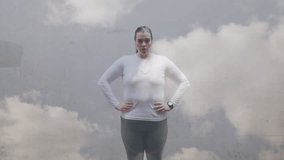 Animation of clouds over plus size caucasian woman in sports clothes flexing muscles. Sports, active lifestyle, urban living and happiness concept digitally generated video.