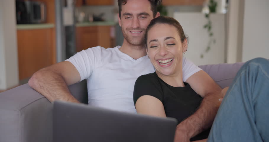 Couple, laptop and laugh on sofa in home to watch movies, streaming multimedia and comedy show online. Happy man, woman and relax in living room at computer, funny video or entertainment subscription Royalty-Free Stock Footage #1108090109