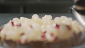 Close up of a chef's hand wearing black gloves laying an pomegranate seeds on top of a longan pie. Decorate the cake. The process of making an longan pie dessert at home in the kitchen. Bakery