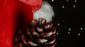 Vertical video. A pinecone lies on Santa's hat with a distant view of a flickering garland in the background. Close-up shot. - Powered by Shutterstock - Get 15% off with code: PIKWIZARD15