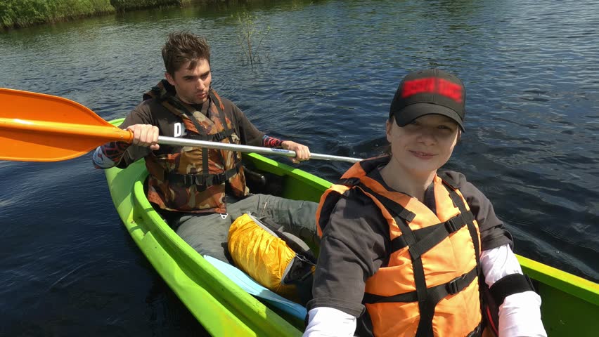 a guy and a girl are sailing on a boat along the river passing through the forest, a man and a woman are sailing in the same boat in a flooded forest, a young couple is actively spending time