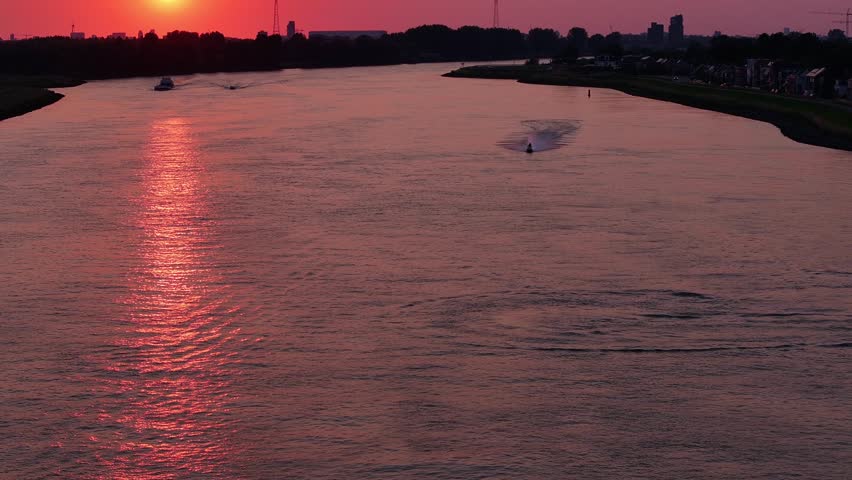 Jet-ski riders speeding along a river under the red sunset of a Rotterdam night