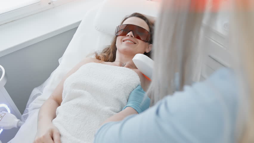 A woman in a beauty salon trusts a cosmetologist during the photoepilation procedure, feeling comfortable and caring. The beautician in the clinic guarantees the safety and effectiveness of laser hair | Shutterstock HD Video #1108106055