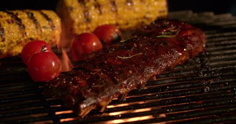 Night time barbecue with tender ribs, small tomatoes and corn grilling over the glowing coals in Slow Motion