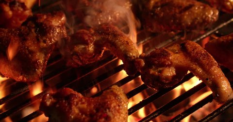 Temptingly spicy chicken wings being grilled over the bright glowing coals of a night time barbecue in Slow Motion