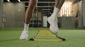 Unknown professional footballer running exercise jumping between ladder sticks male sportsman man soccer player muscular legs in sneakers fast jogging in sport gym training workout on football pitch - Powered by Shutterstock - Get 15% off with code: PIKWIZARD15