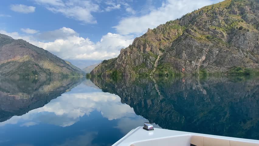 A walk on a white boat on the cold transparent mountain lake of Sary Chelek. Majestic cliffs, mountains, ridges, hills and peaks. The State Biosphere Reserve is a specially protected natural territory