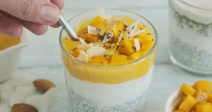 Person eating chia pudding with mango, yogurt and chia seeds. Creamy smoothie dessert, healthy raw dessert, close-up video clip, horizontal footage 4k