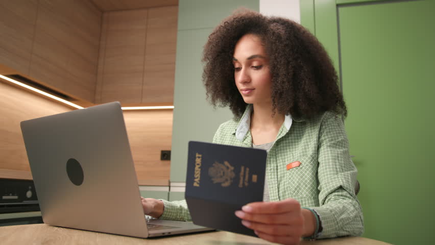 Woman Typing on Laptop Holding US Passport. Black female working holding US passport document. Royalty-Free Stock Footage #1108115511
