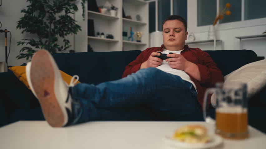 Young man playing video game and drinking beer at home, weekend activities