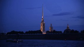 Side view from tour boat of illuminated Russian Orthodox Saints Peter and Paul Cathedral at night in Saint Petersburg, Russia. Religious architecture. Real time handheld video. Water tourism theme.