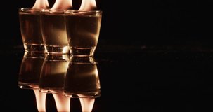 Video of lit alcohol in glasses with yellow fire flames and copy space on black background. Fire, flames, heat and light concept.