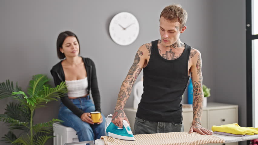 Beautiful couple smiling confident ironing clothes drinking coffee at laundry room