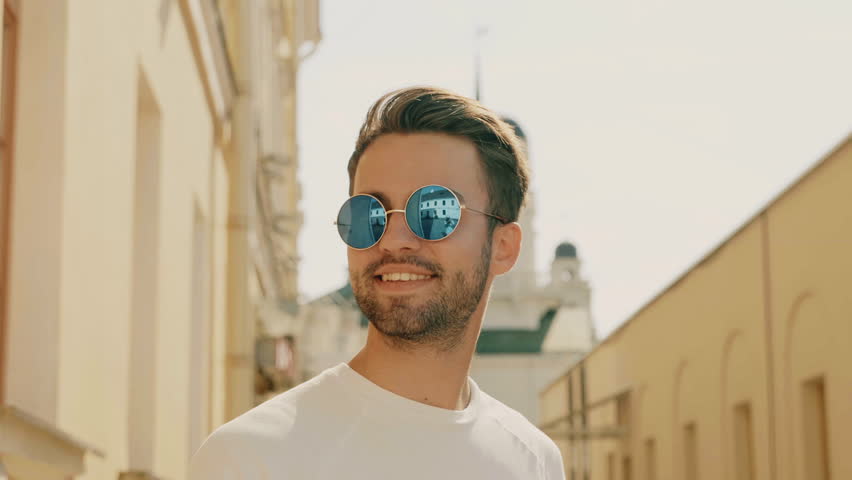 Portrait of handsome stylish hipster lambersexual model. Man dressed in T-shirt. Fashion male posing in the street outdoors in sunglasses