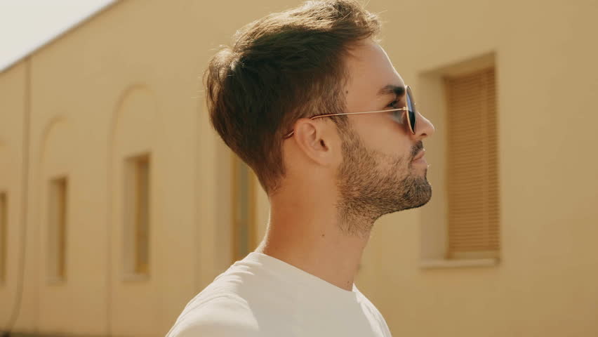 Portrait of handsome stylish hipster lambersexual model. Man dressed in T-shirt. Fashion male posing in the street outdoors in sunglasses