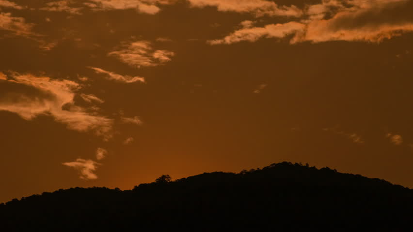 Time lapse of the sun setting over hills that are covered with clouds, in the style of smokey background.