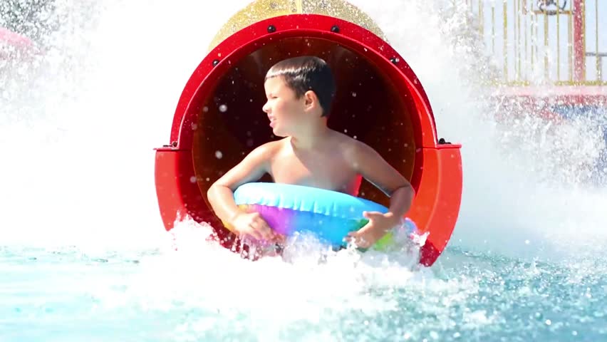 Smiling cheerful child rides down a red tube water slide in a water park on vacation