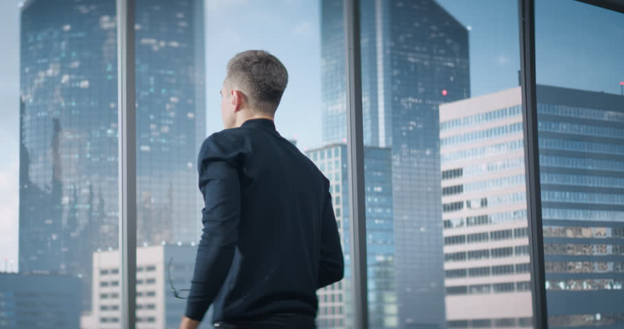 Caucasian Businessman Sitting Down At His Desk And Starts Typing On Laptop Computer In Corner Office With Megapolis Cityview. Proffesional Digital Entreprenuer Working With Ecommerce.