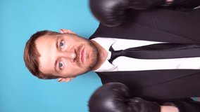 Young businessman in suit and boxing gloves over blue background. Fighting for business success. Looking at camera. Vertical video.