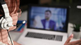 online conference, young female employee with a headset communicates with boss via video link on a laptop while sitting at a table in room