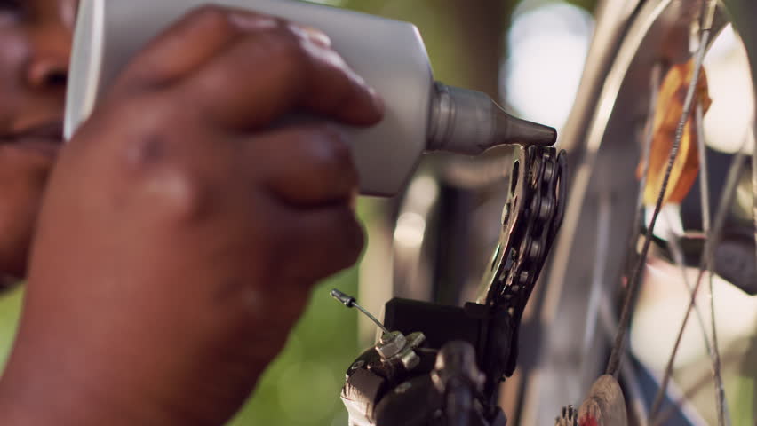 Sports-loving black woman cautiously greasing and maintaining her bike disc brake ring outside. Close-up view of female carefully lubricating rusty bicycle with specialized chain lubricant. Royalty-Free Stock Footage #1108132849