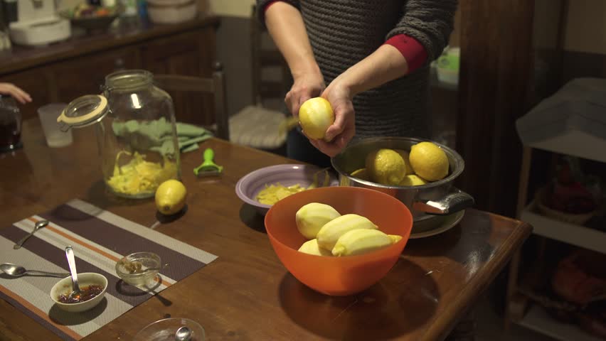 Homemade alcoholic drink limoncello in the home kitchen in the Italian village. Woman peeling lemon skin using a peeler 4K