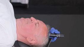 A trichologist conducts a detailed hair diagnosis and examination of an older man. Vertical video