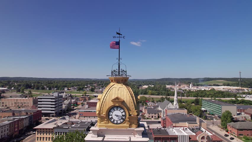 Establishing aerial view and drone shot rotating around American flag and compass on top of government clocktower and tall building structure in the middle of the small town America of Newark, Ohio