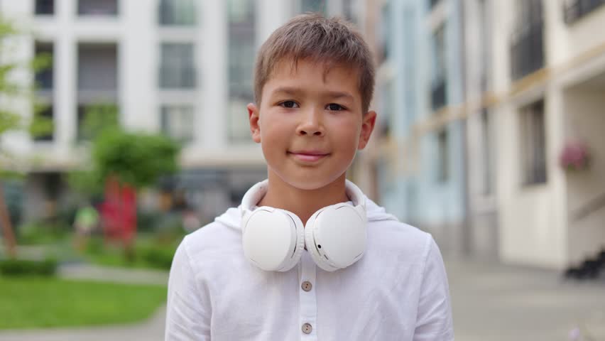 Handsome Boy Putting On the Big White Headphones while Standing Outside. Cute Young Guy Outdoors Wearing Headphones, Getting Ready Listen to Music. People and Technology Concept
