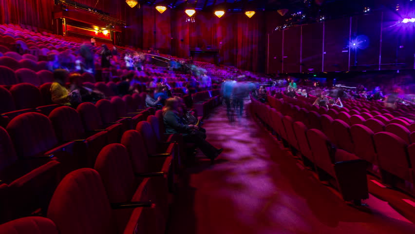 Spectators gather in the auditorium and watch the show in theatre timelapse. Large hall with red armchairs seats. Viewers filling places until turn off the light. Panoramic view from left side