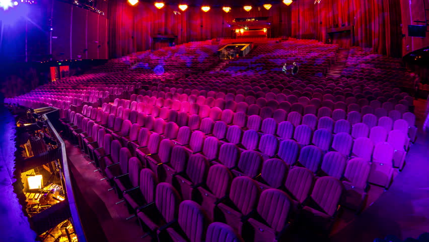 Spectators gather in the auditorium and watch the show in theatre timelapse. Large hall with red armchairs seats. Viewers filling places until turn off the light. View from a stage Royalty-Free Stock Footage #1108142357