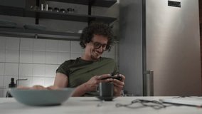 One adult caucasian man sit at home happy smile play video games leisure activity having fun hold mobile phone smartphone have fun copy space wear eyeglasses and shirt slow motion