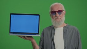 Green Screen.Portrait of an Old Man in the Funny Glasses Pointing at His Laptop With a Blue Screen. Online Shopping for Seniors. Smart Homes and the Internet of Things for Seniors.
