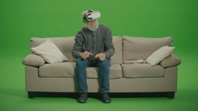 Green Screen. An Old Man With Gray Beard in VR Glasses Examines and Touches Everything Around, Sitting on a Sofa. VR for the Socialization of the Elderly. VR to Help the Elderly with Disabilities. - Powered by Shutterstock - Get 15% off with code: PIKWIZARD15