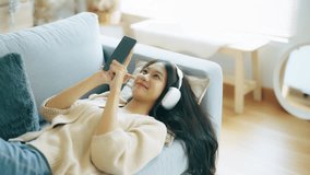 Happy young asian woman relaxing at home. Female smile lying on sofa and holding mobile smartphone. Girl using video call to friend
