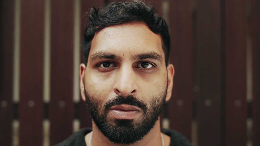 Portrait of Adult Arabic Man Looking at Camera on Wooden Wall Background. One Smiling Face and Beautiful Eyes of Happy Arabian Person Outdoors. Optimism of Successful Young Male Standing at Wood Fence
